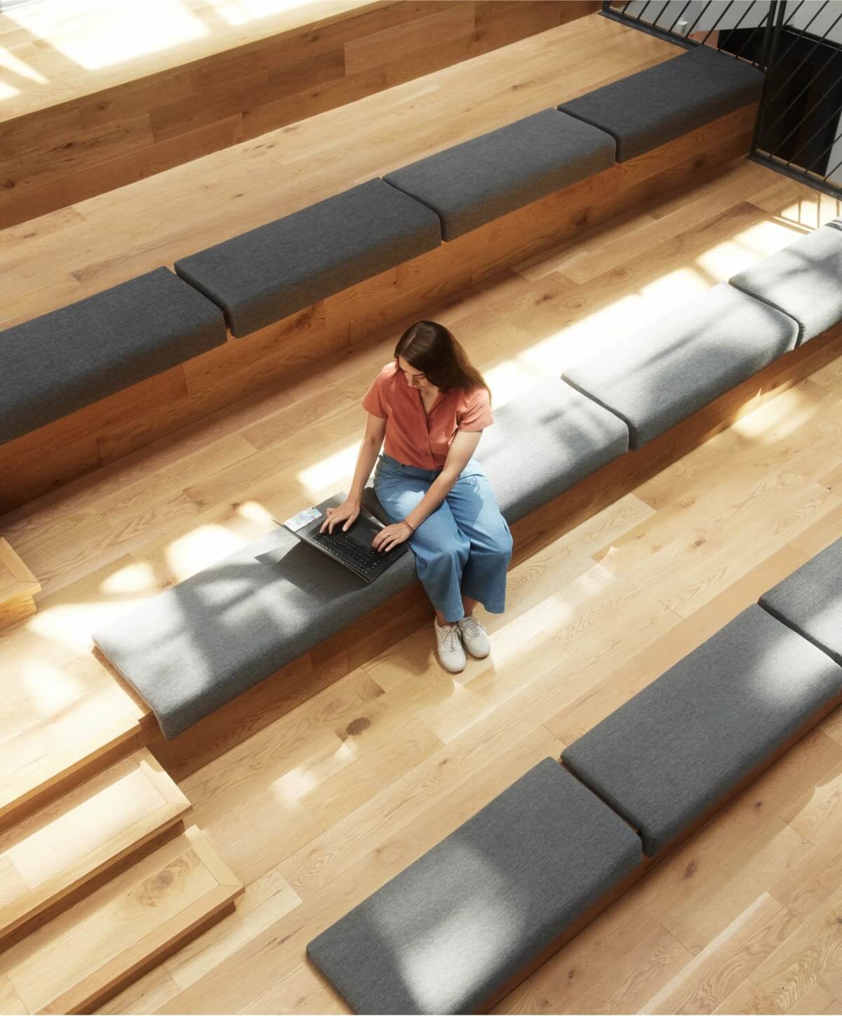 Overhead view of an employee working on her laptop alone in a sunny auditorium at the Workleap office.