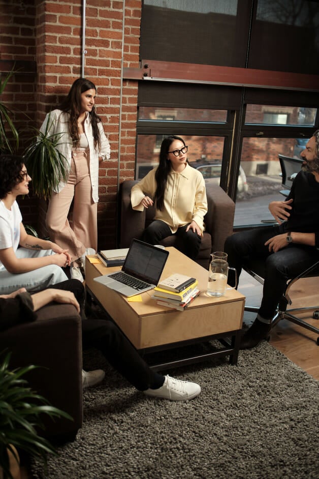 Employees casually sit in discussion around coffee table at office.