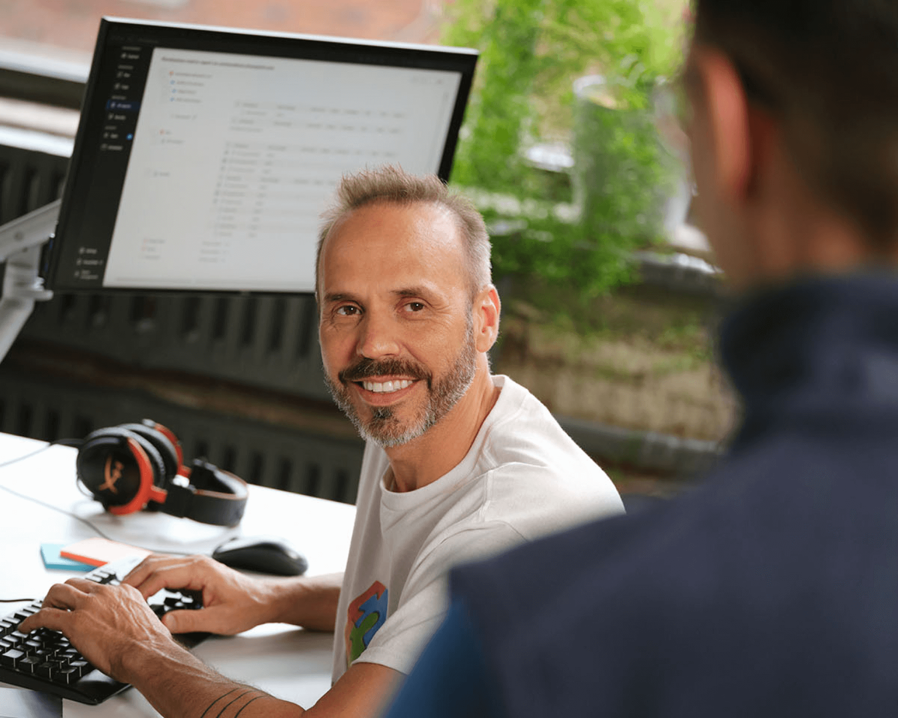 A smiling IT specialist talking to their manager at their desk, reflecting job satisfaction.